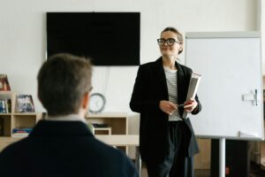 A Woman in a Black Blazer and Eyeglasses Standing in a Classroom